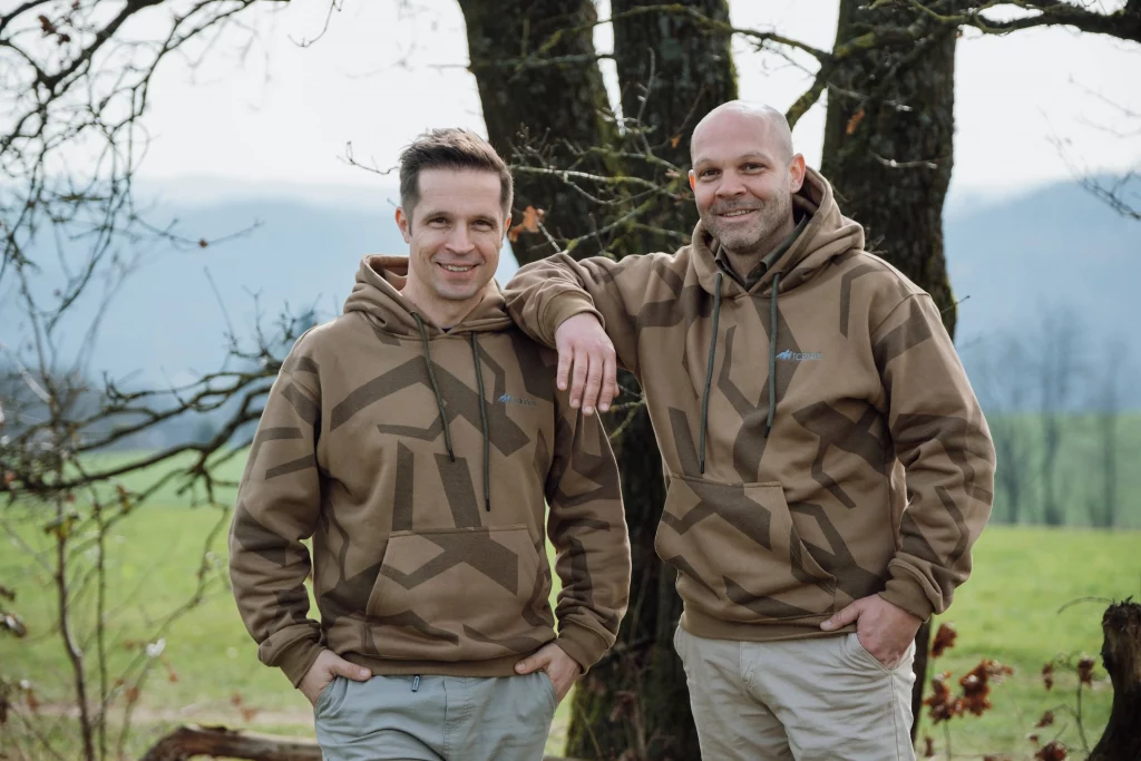 Dr. Tino und Nico Kessler-Thönes stehen in braunen Hoodies vor einem Baum in der Natur und schauen in die Kamera, Gründer der Hochsitz Akademie