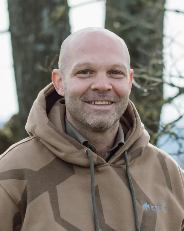 Nico Kessler-Thönes steht in einem braunen Hoodie vor einem Baum mit natürlichem Hintergrund und lächelt in die Kamera, Jagdausbilder der Hochsitz Akademie