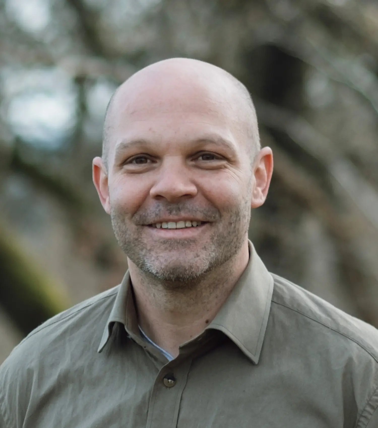 Nico Kessler-Thönes lächelt in die Kamera und trägt ein grünes Hemd, unscharfer Hintergrund mit Bäumen, Geschäftsführer der Hochsitz Akademie